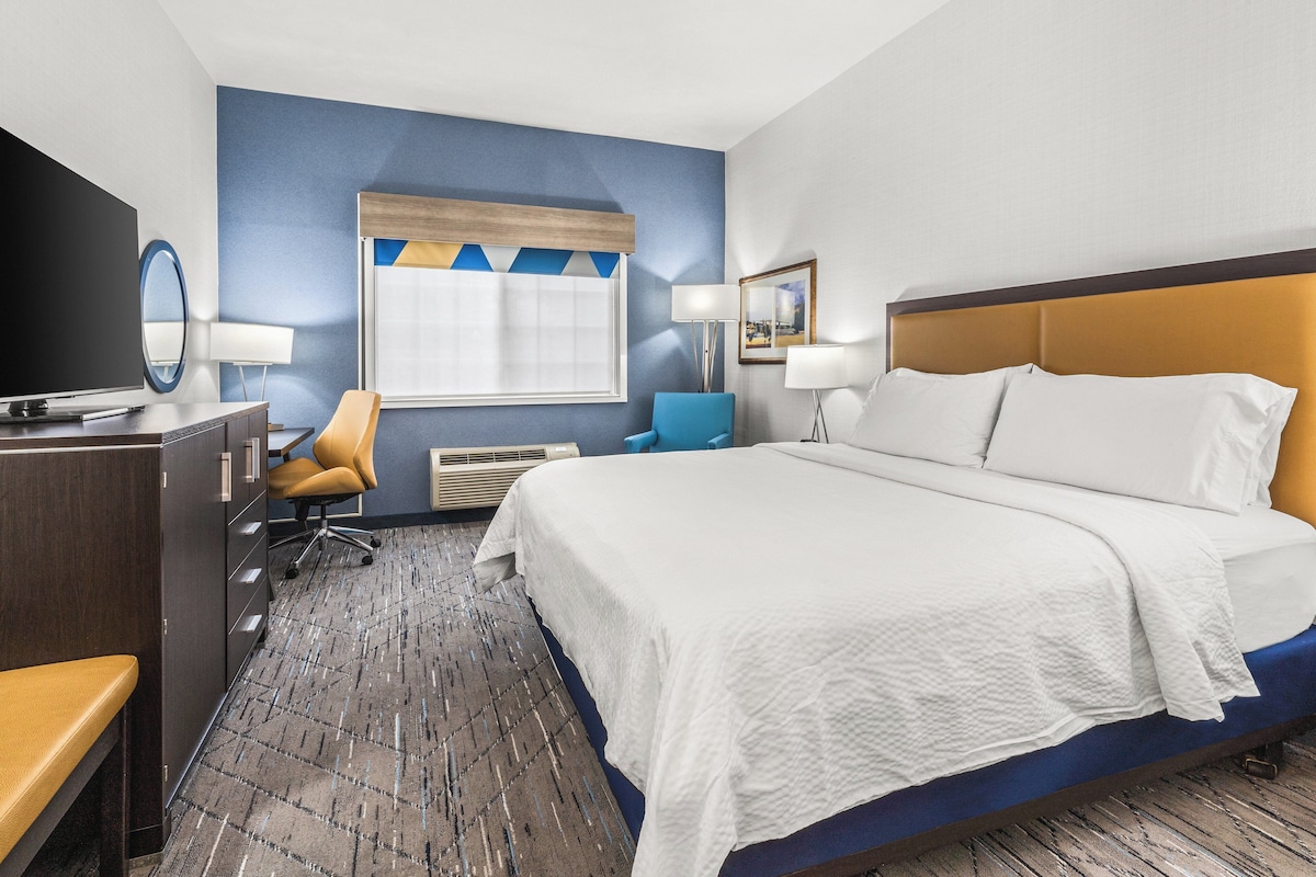 A hotel room with a bed, a desk, a chair, a television, and a window.