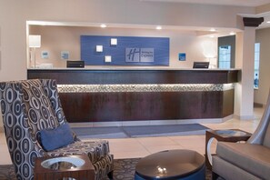 A hotel reception area with a modern design, including a reception desk, seating area with patterned chairs, and a glass coffee table.