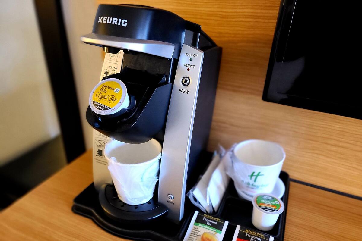 A Keurig coffee machine with a cup holder, two disposable cups, and two sachets of tea.