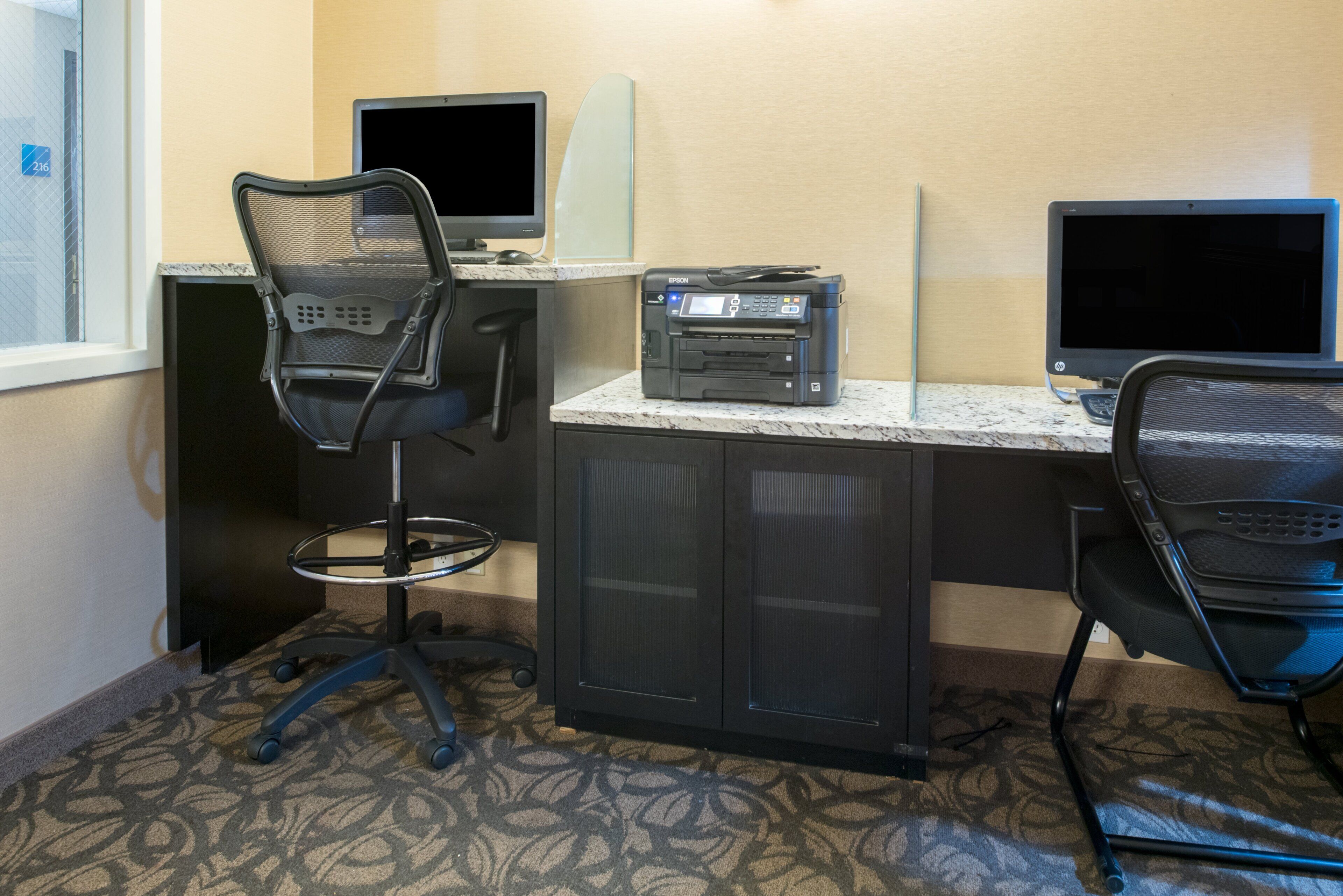 Habitación de hotel con escritorio, dos monitores, una impresora y una silla.