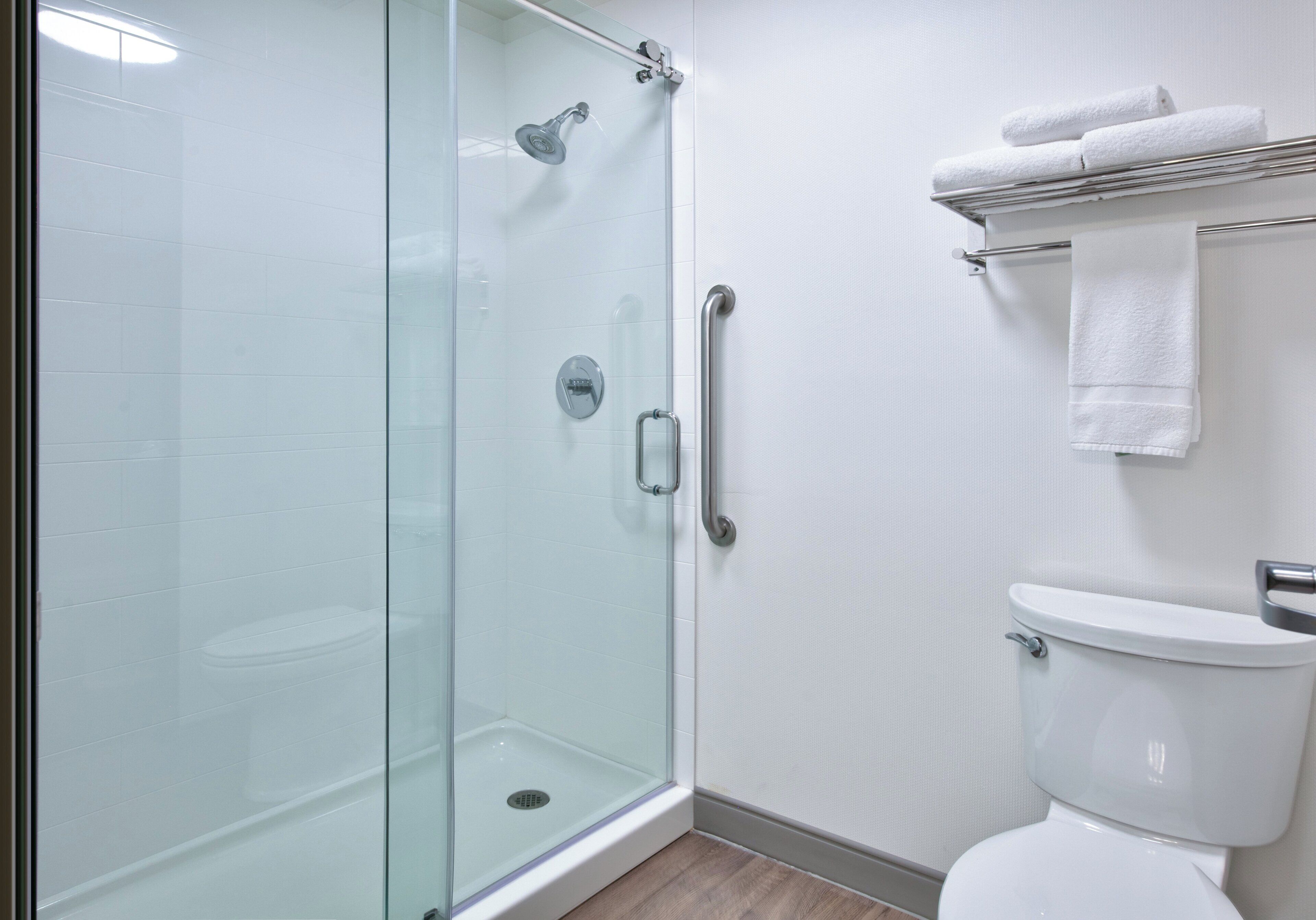 A modern bathroom with a glass-enclosed shower, a white toilet, and a towel rack with folded towels.