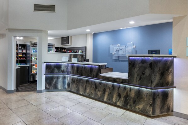 A reception area with a curved counter, a blue wall, and a refrigerator stocked with beverages. - Holiday Inn Express Spokane-Valley by IHG (Spokane Valley)