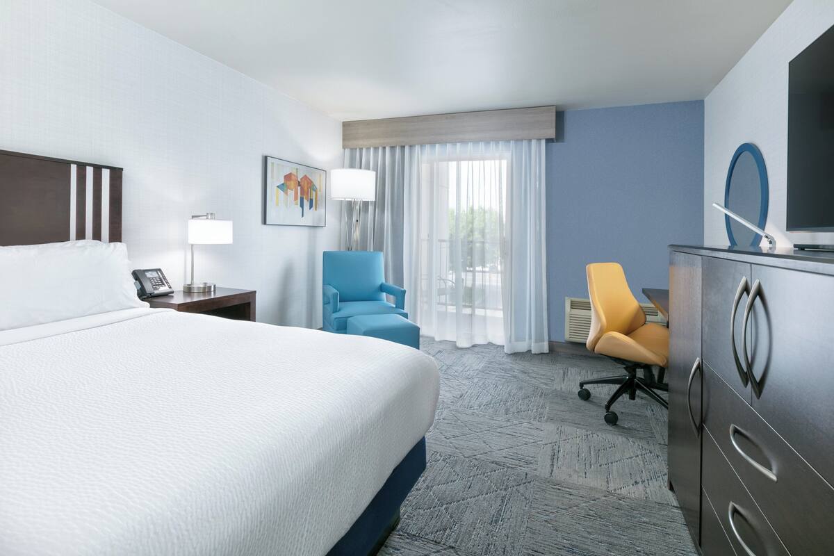 A hotel room with a large bed, a desk with a chair, a TV, and a window with curtains.