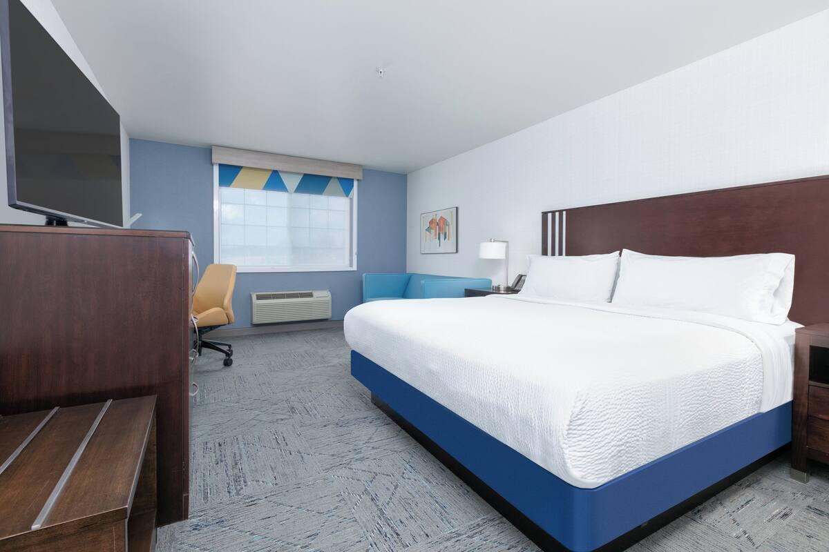 A hotel room with a large bed, a desk, a chair, a TV, and a window with a view.