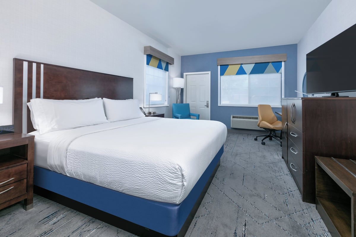 A hotel room with a large bed, a desk, a chair, a TV, and a wardrobe.