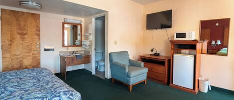 A hotel room with a bed, a desk, a chair, a television, a microwave, and a small refrigerator.