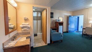 A hotel room with a bathroom, a bed, a desk, and a TV. - Travelers Inn by OYO Longview Kelso (Longview)
