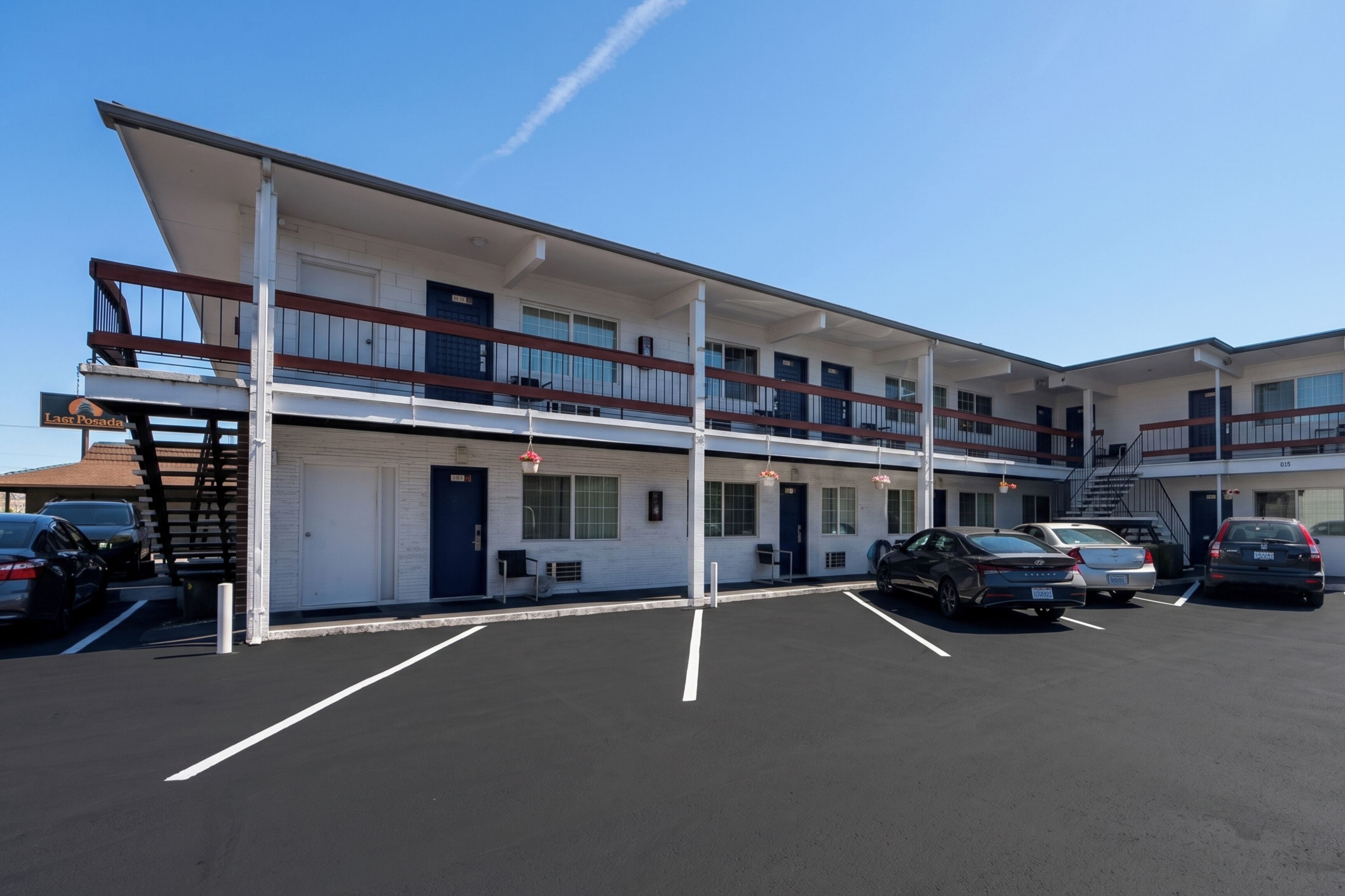 A motel with a two-story structure, a parking lot, and several cars parked.