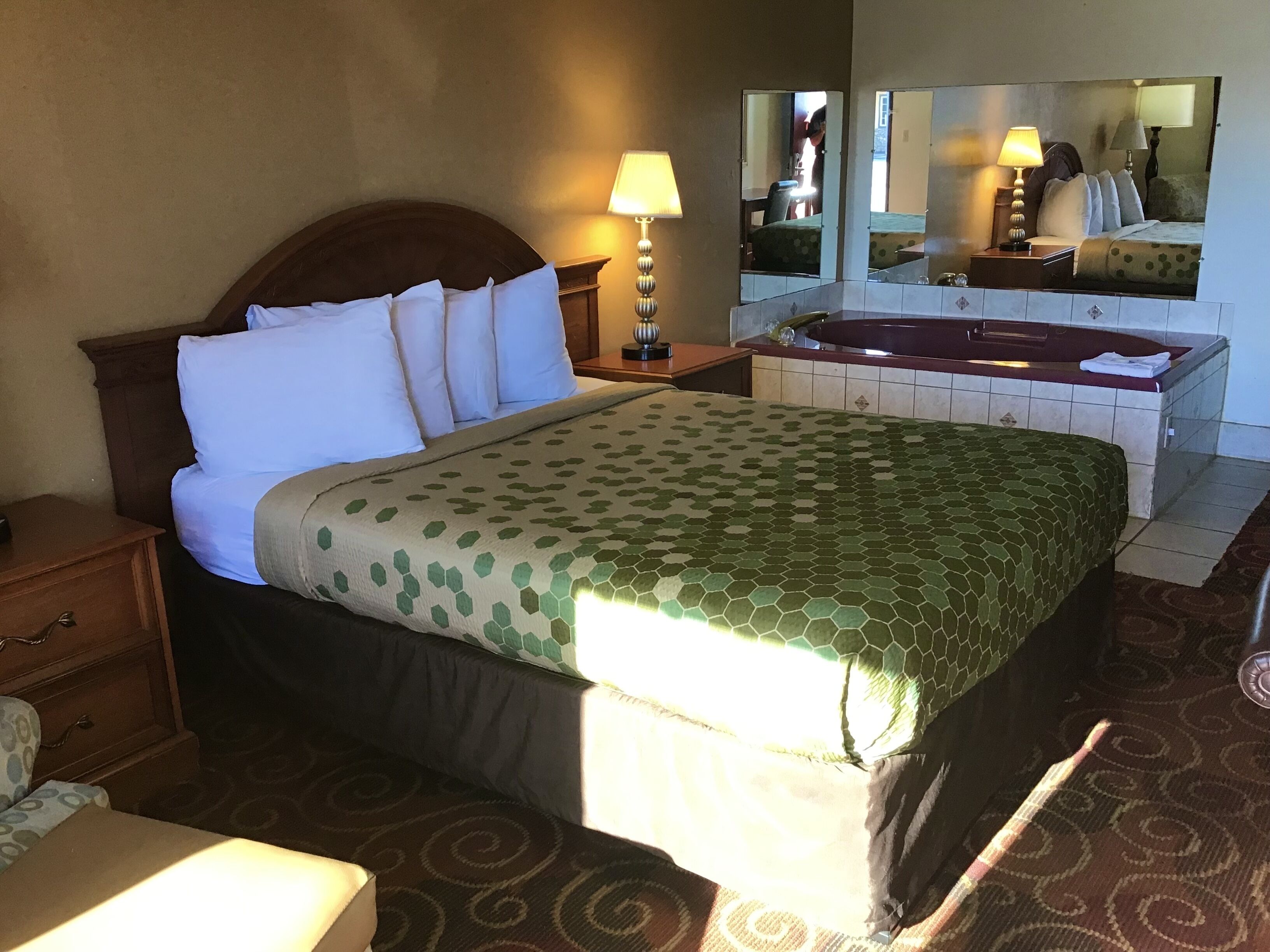 A hotel room with a large bed, a sitting area, a bathroom with a bathtub, and a mirror reflecting the room.