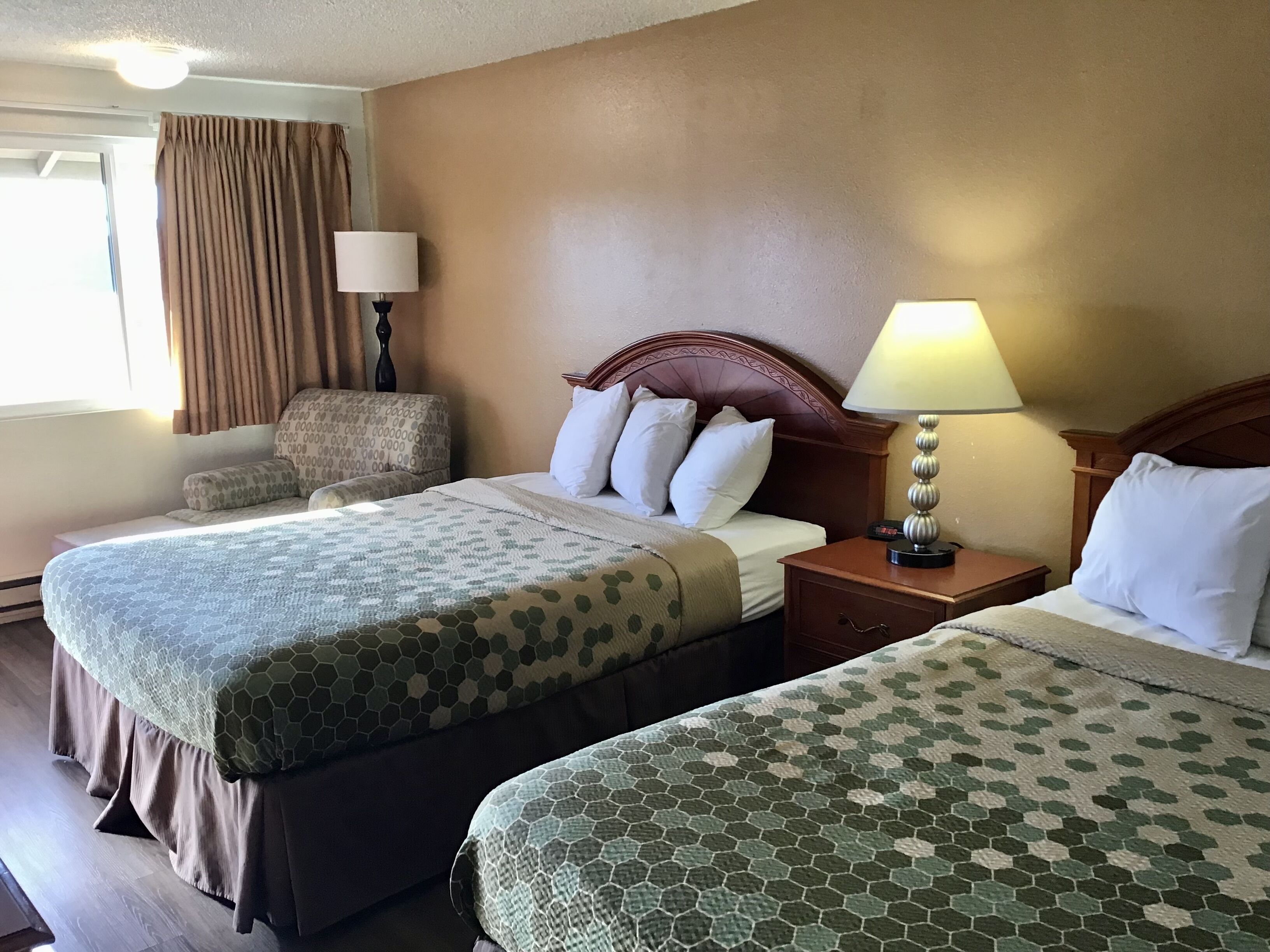 A hotel room with two beds, a nightstand, a lamp, a chair, and a window with curtains.