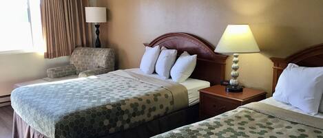 A hotel room with two beds, a nightstand, a lamp, a chair, and a window with curtains.