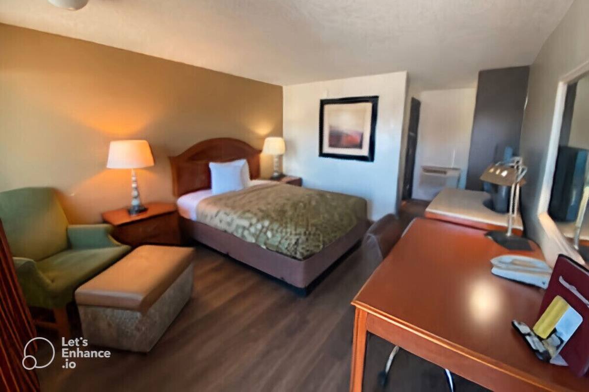 Habitación de hotel con cama, escritorio, silla, lámpara y un cuadro en la pared.
