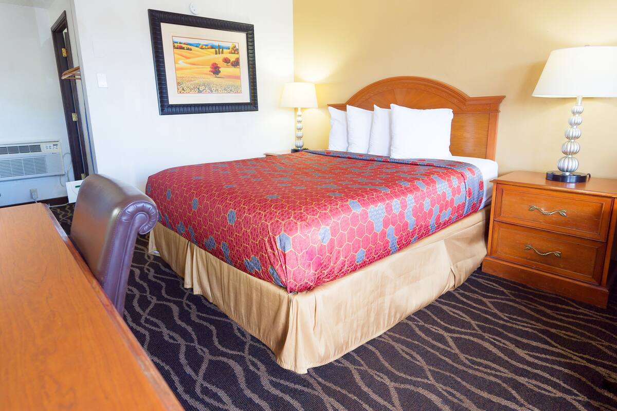 Habitación de hotel con cama, escritorio, silla, mesita de noche y lámpara.