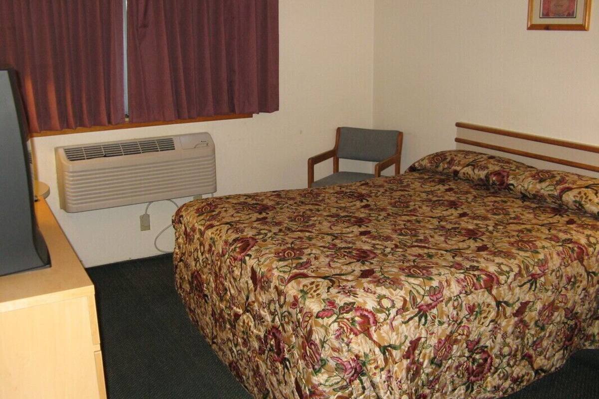 A bedroom with a bed, a chair, a television, and an air conditioner.