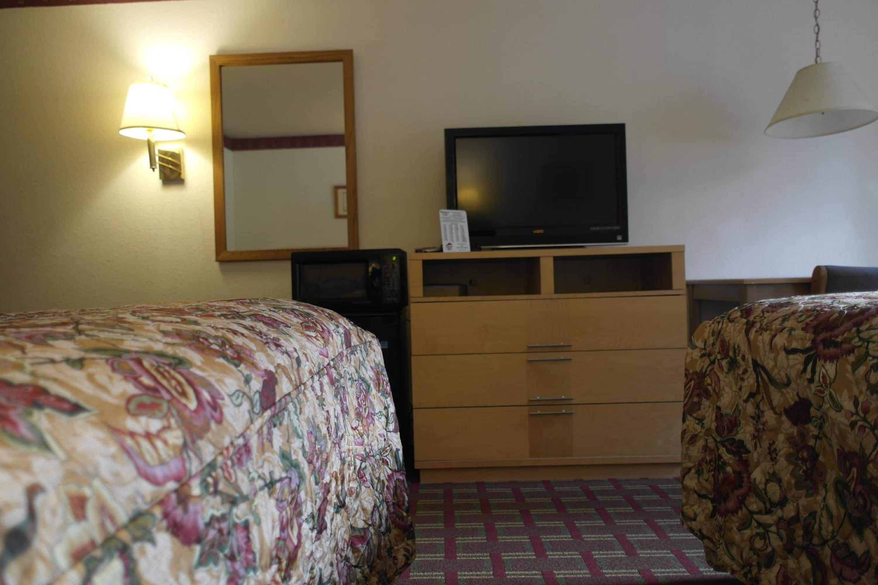 Ein Hotelzimmer mit zwei Betten, einem Fernseher auf einer Holzkommode und einer Pendelleuchte.