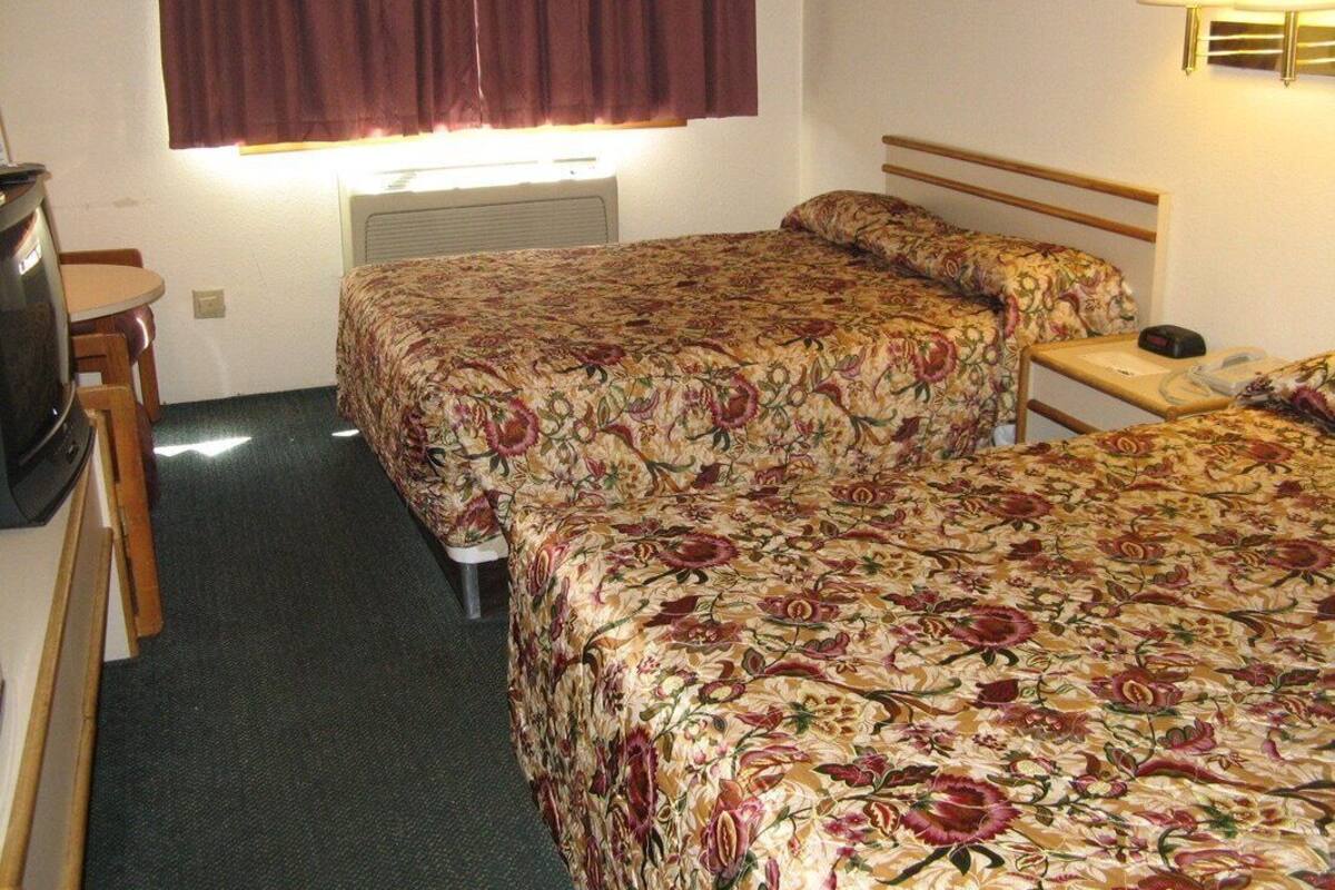 A hotel room with two beds, a desk, a chair, a lamp, and a window with curtains.