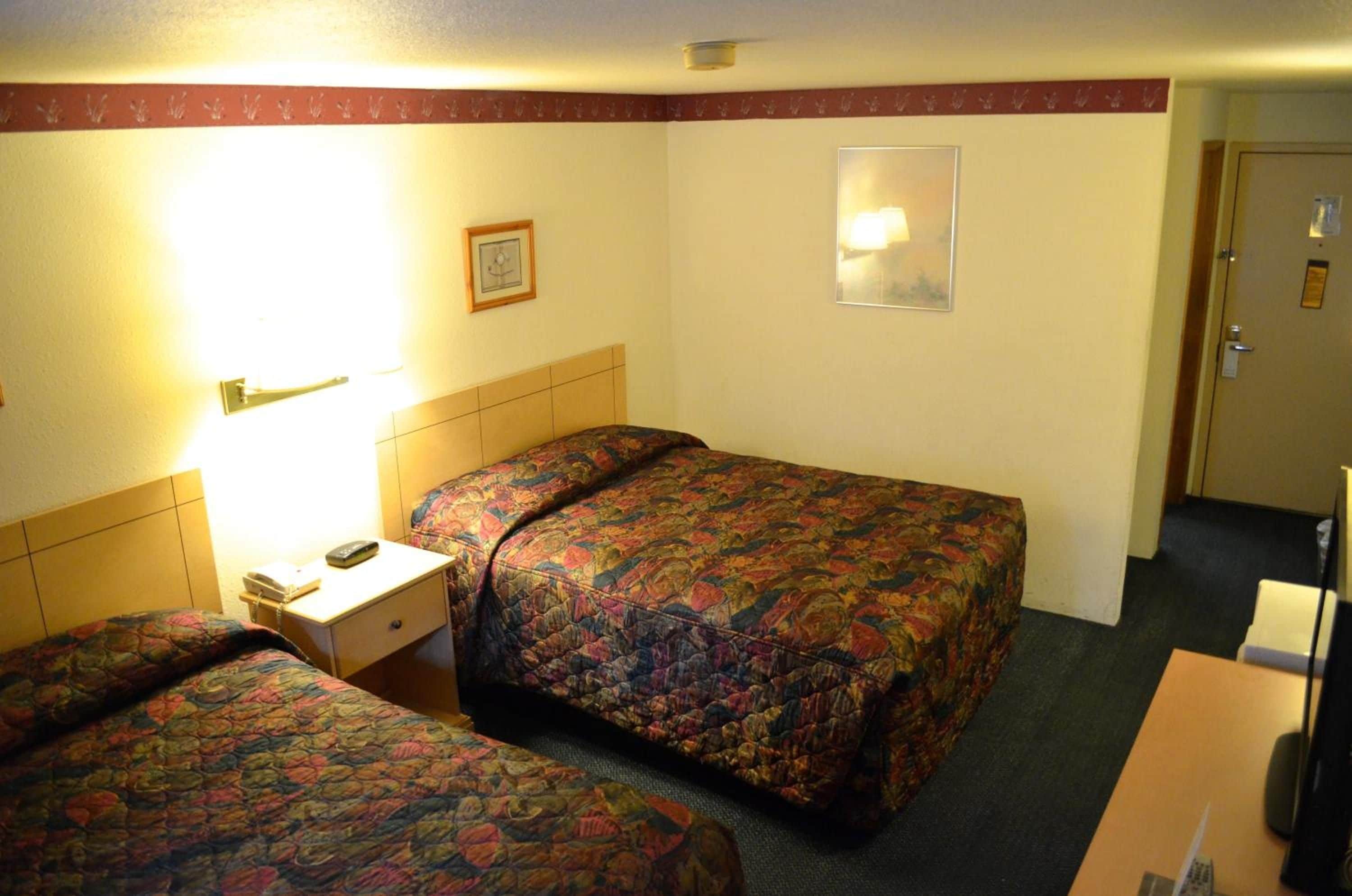 Habitación de hotel con dos camas, una mesita de noche con lámpara, un escritorio pequeño y una puerta.