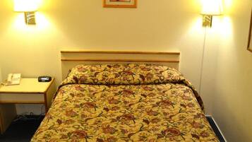 Ett hotellrum med ett blommigt sängöverkast, två sänglampor, ett nattduksbord med en telefon och en inramad tavla på väggen.