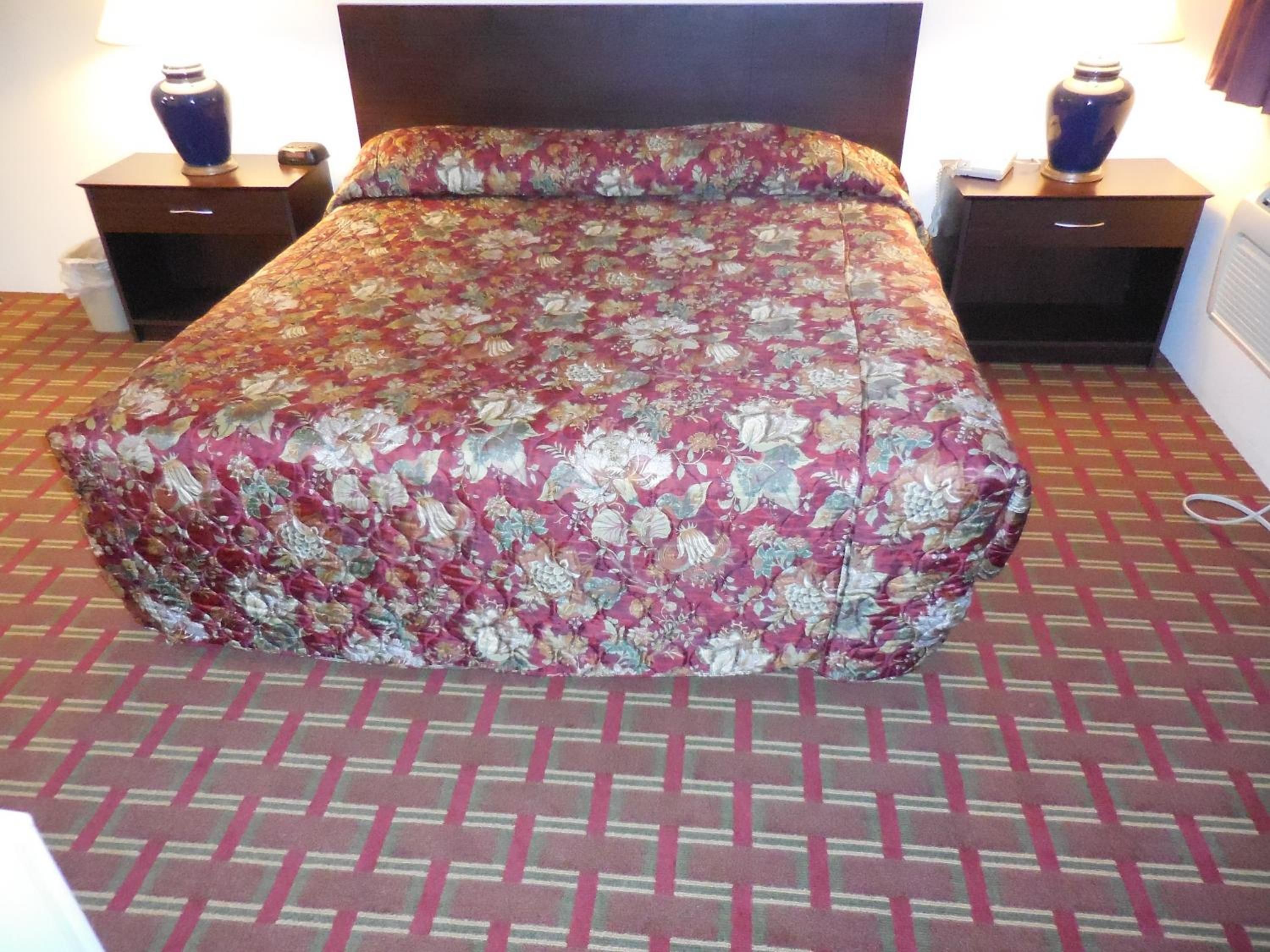 Un lit recouvert d’une couvre-lit à motifs floraux, deux tables de chevet avec des lampes et un tapis à motifs.
