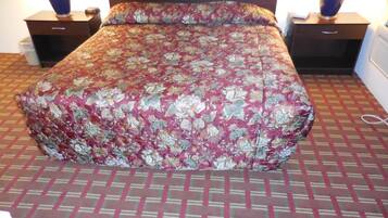 Un lit recouvert d’une couvre-lit à motifs floraux, deux tables de chevet avec des lampes et un tapis à motifs.