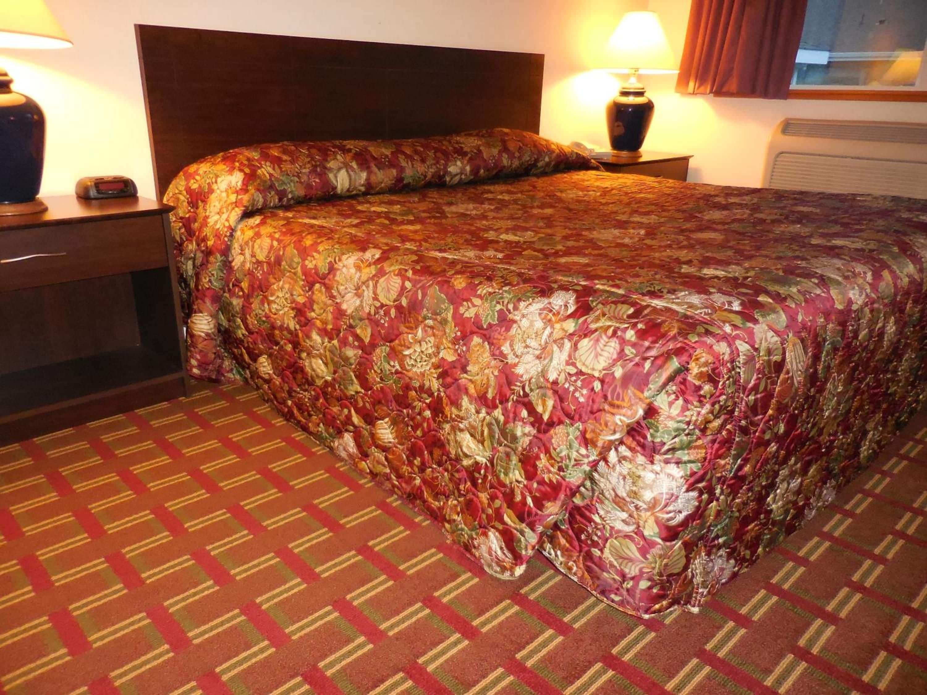 A hotel room with a large bed, a nightstand with a lamp, and a window with curtains.