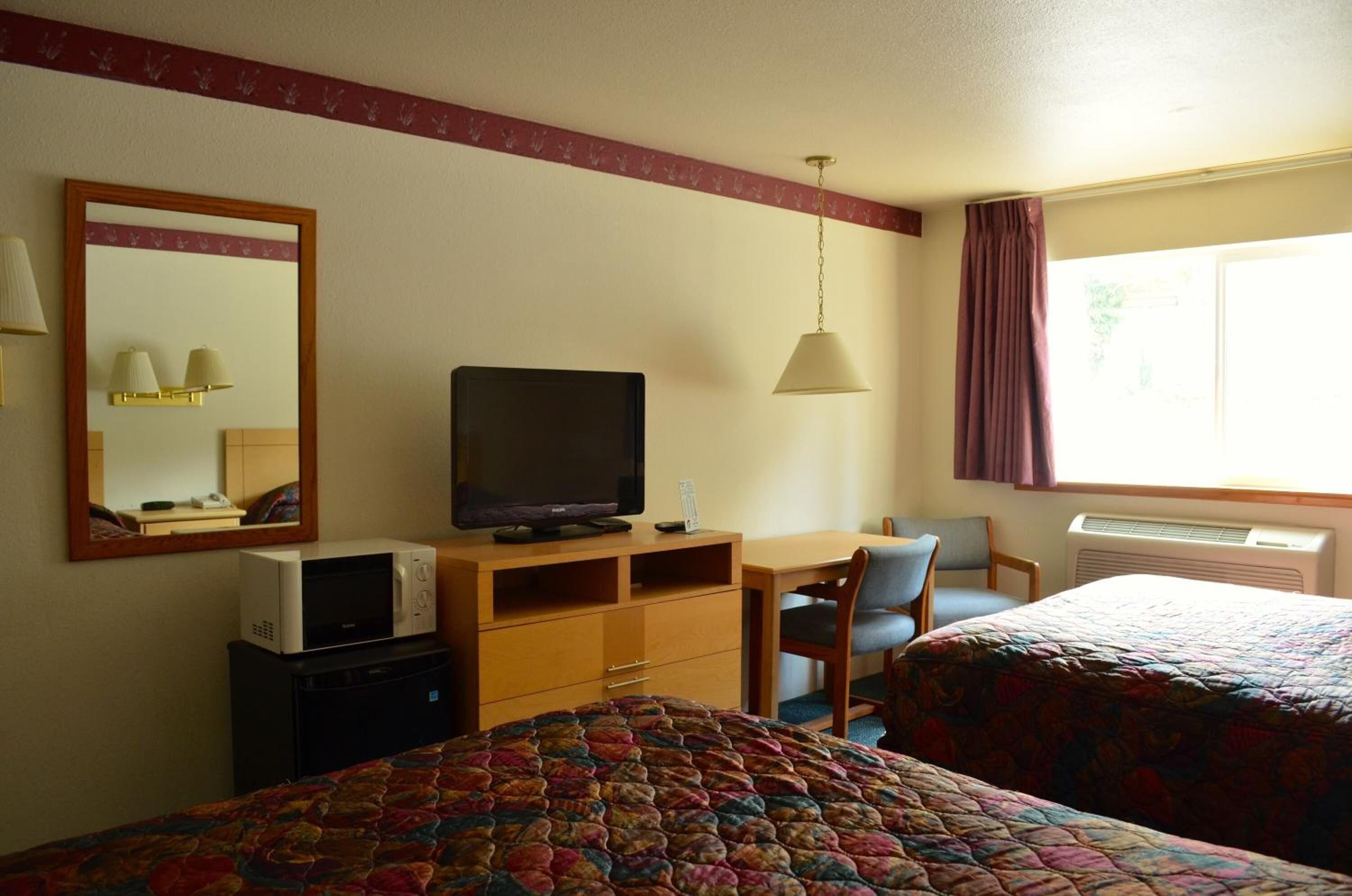 A hotel room with a bed, a desk with a television, a chair, a microwave, and a window with curtains.