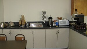 A kitchen with a table, chairs, a coffee machine, a microwave, and various kitchen items on the counter.