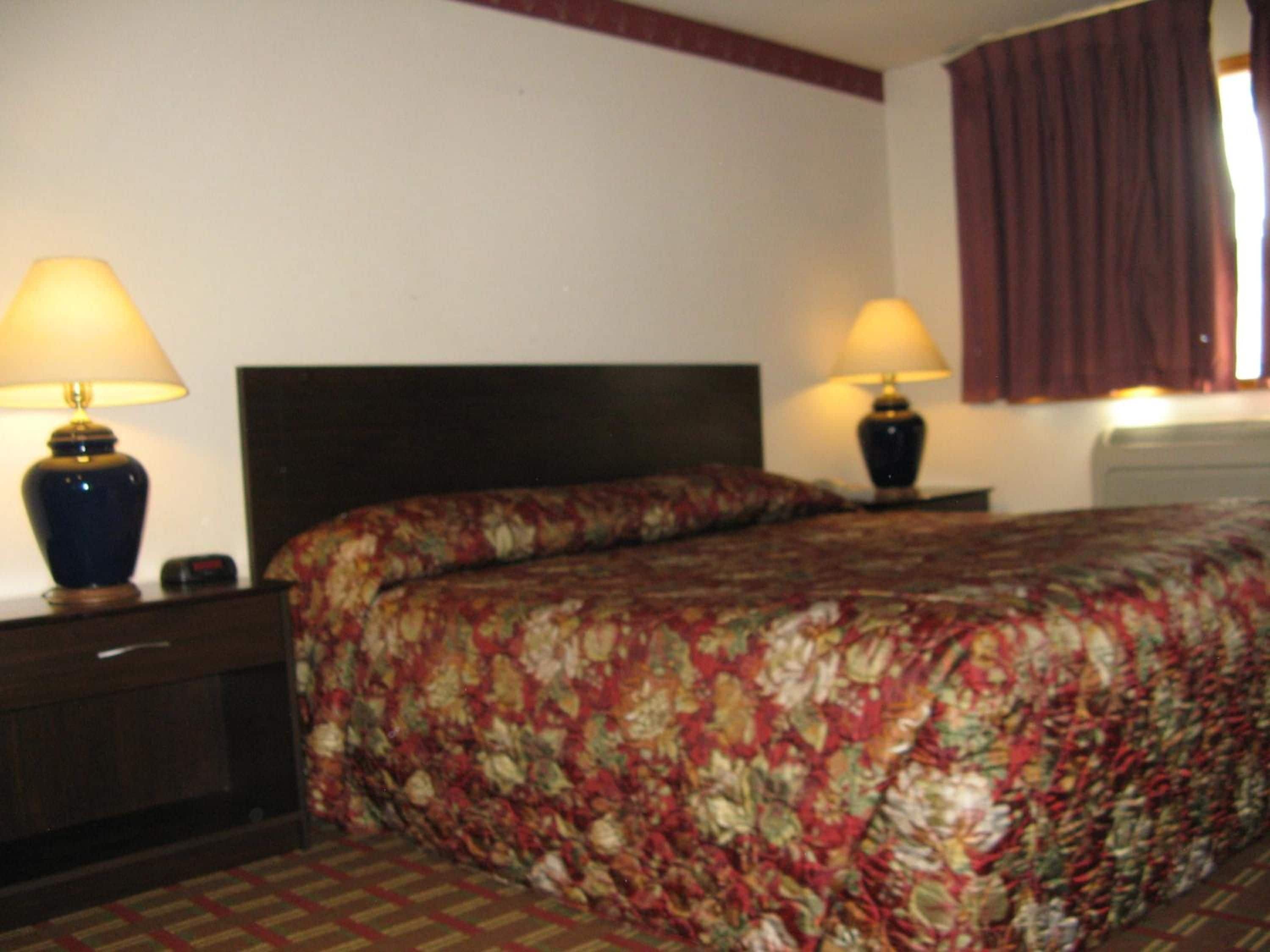 A hotel room with a bed, two bedside lamps, a nightstand, and a window with curtains.