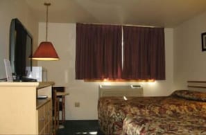 Una habitación pequeña y sencilla con cama, escritorio, silla y televisión.