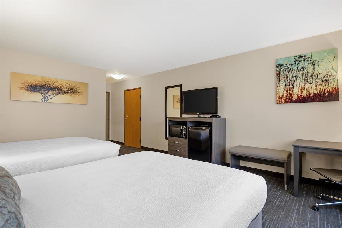 A hotel room with two beds, a desk, a television, and artwork on the walls.