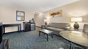 A hotel room with a sofa, a glass table, a coffee station, and a painting on the wall. - Best Western Plus City Center (Spokane)