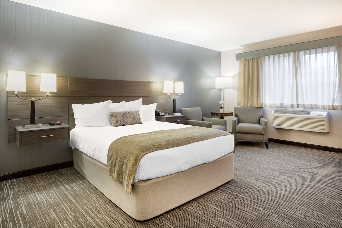 A hotel room with a large bed, two bedside tables with lamps, a chair, and a window with curtains.