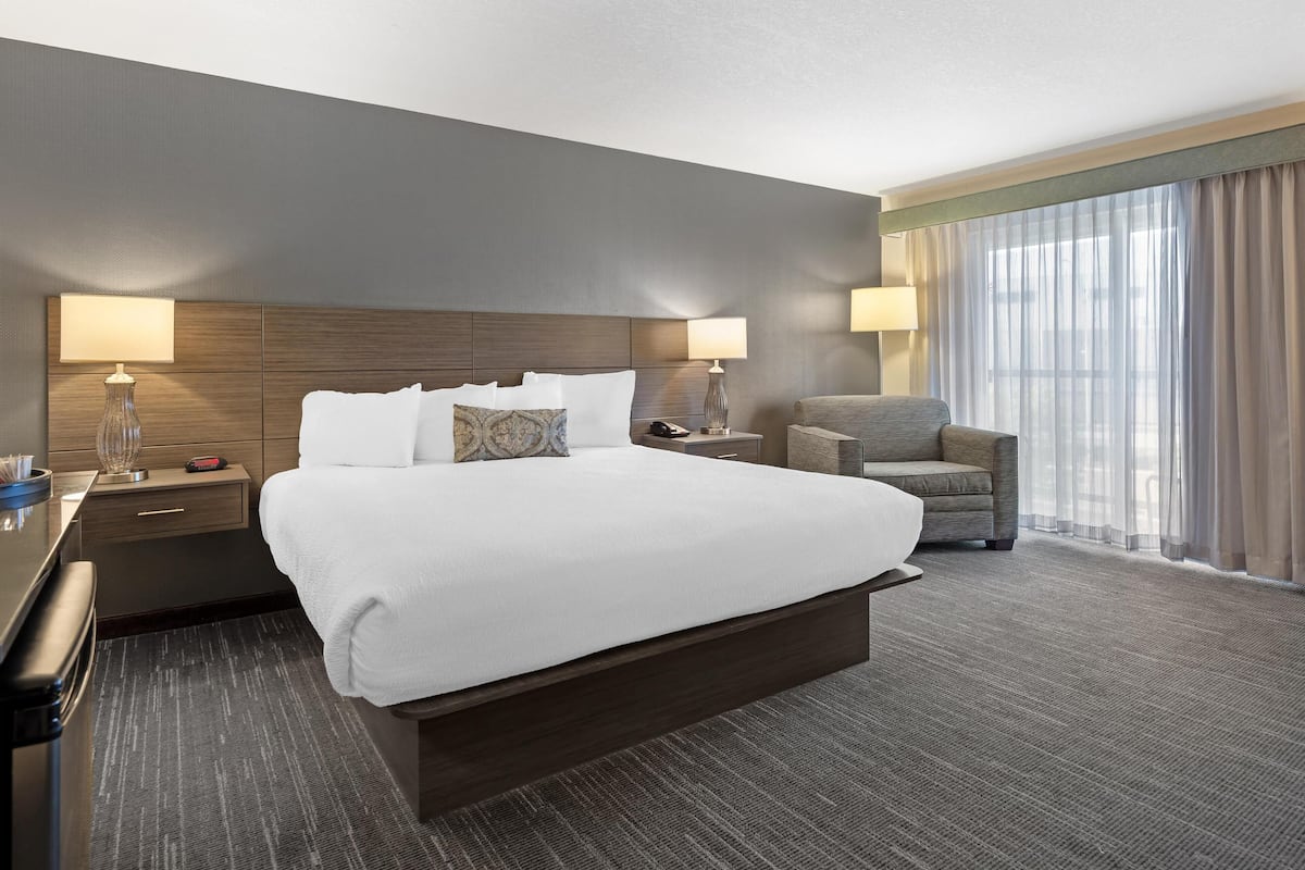 A hotel room with a large bed, two bedside tables, a chair, and a large window with curtains.