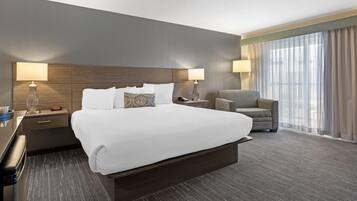 A hotel room with a large bed, two bedside tables, a chair, and a large window with curtains.