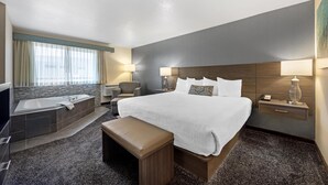 A hotel room with a large bed, a sitting area with a chair, a small table, a bedside lamp, a telephone, and a window with curtains. - Best Western Plus City Center (Spokane)