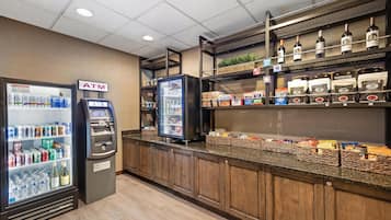 A self-service kiosk area with an ATM, refrigerated display cases, and shelves stocked with snacks and bottled water.