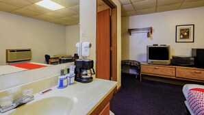 A hotel room with a large mirror, a sink, a coffee maker, a television, and a microwave.
