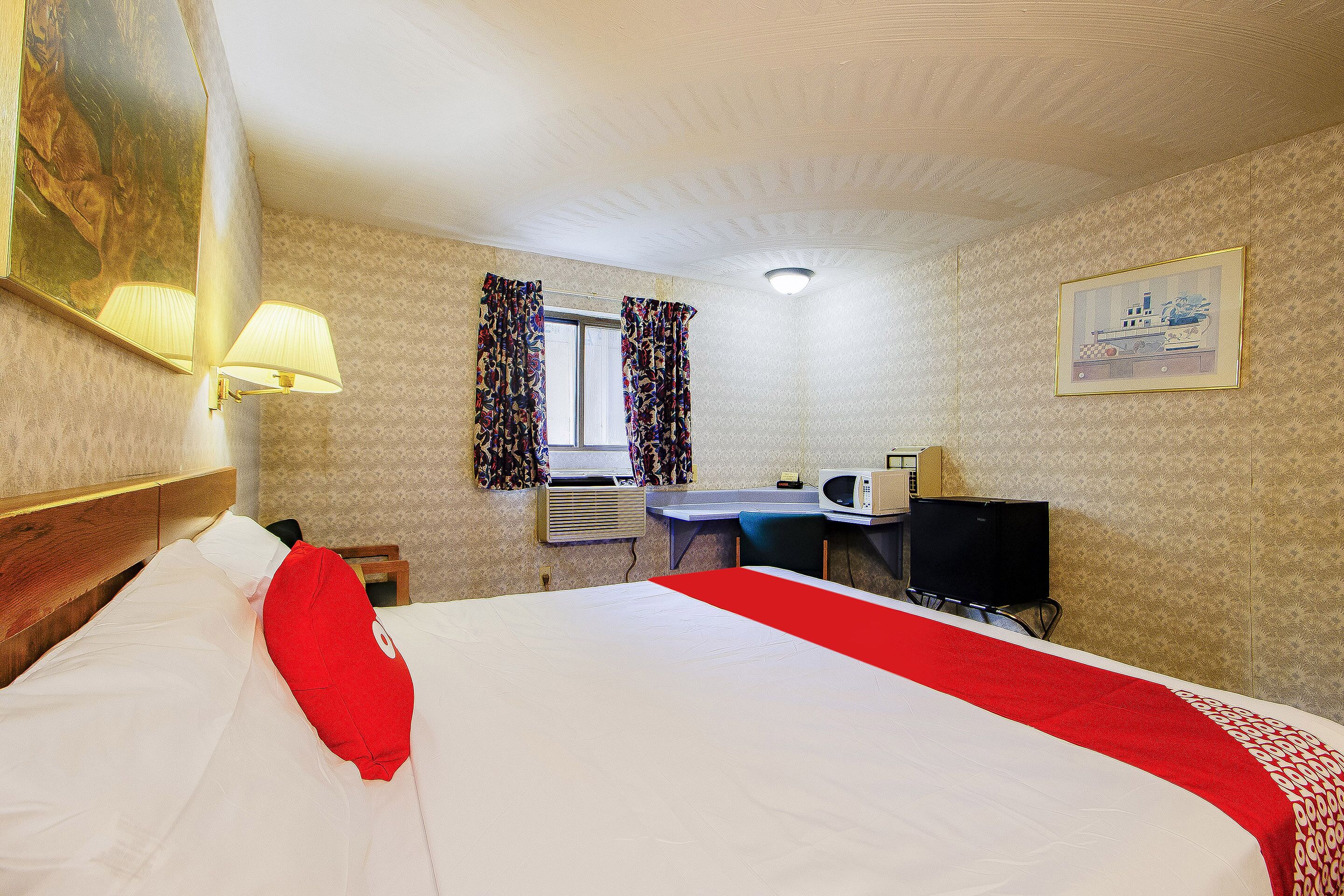 A hotel room with a bed, a desk, a television, and a window with curtains.