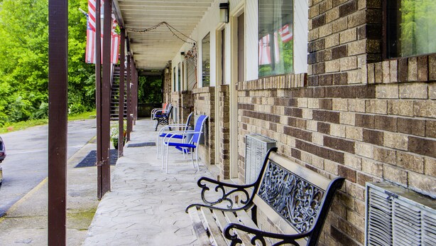A covered outdoor seating area with benches and chairs, a brick building, and American flags.