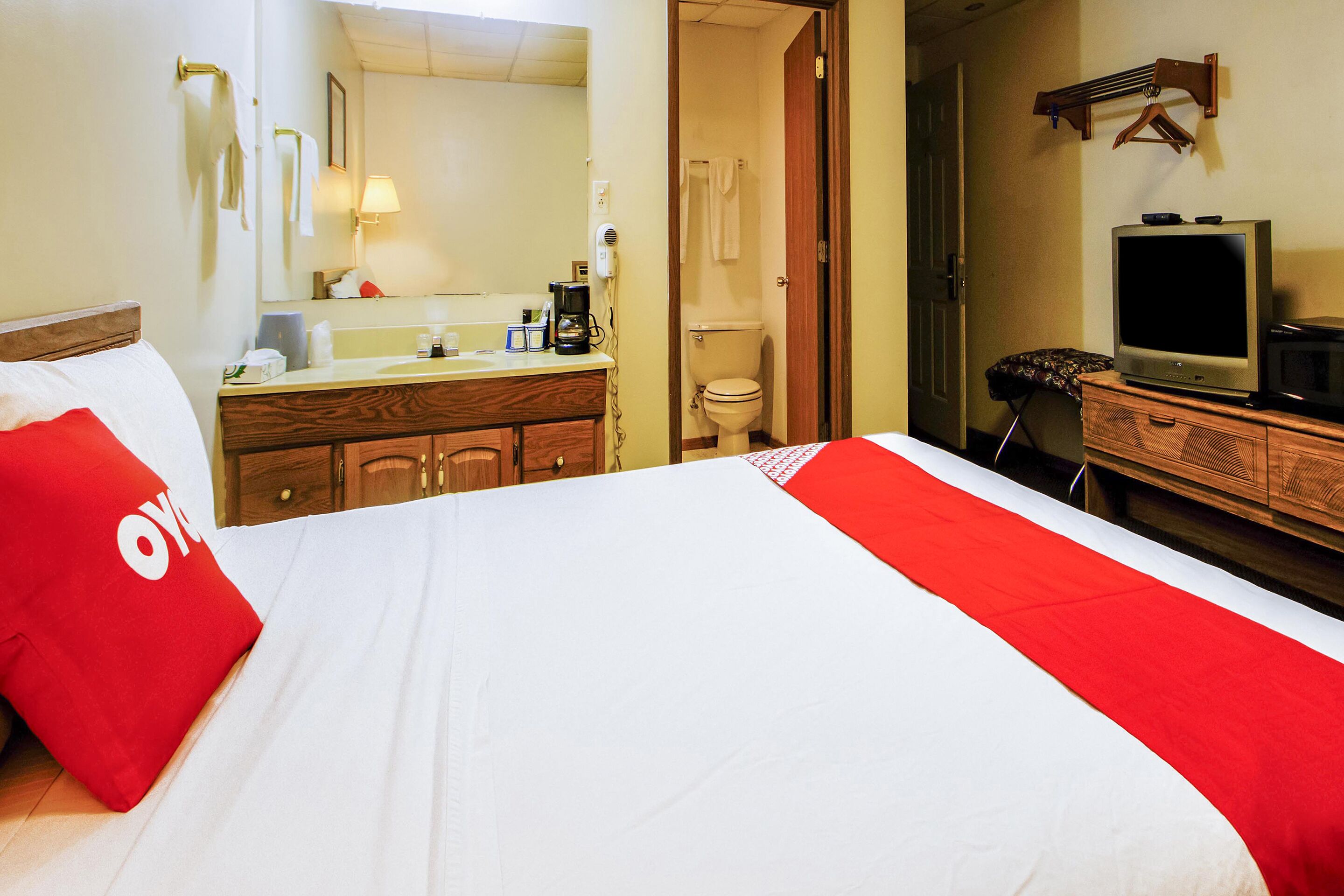 A hotel room with a bed, a wooden dresser, a television, and a bathroom visible through an open door.