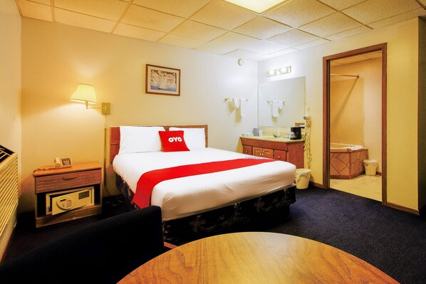 A hotel room with a bed, bedside table, lamp, and a small table.