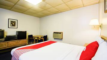 Una habitación de hotel con cama, escritorio, silla, televisor y aire acondicionado.