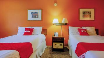 Quarto de hotel com duas camas, cada uma com almofada vermelha da OYO, roupa de cama branca e mesa de cabeceira com abajur e telefone.
