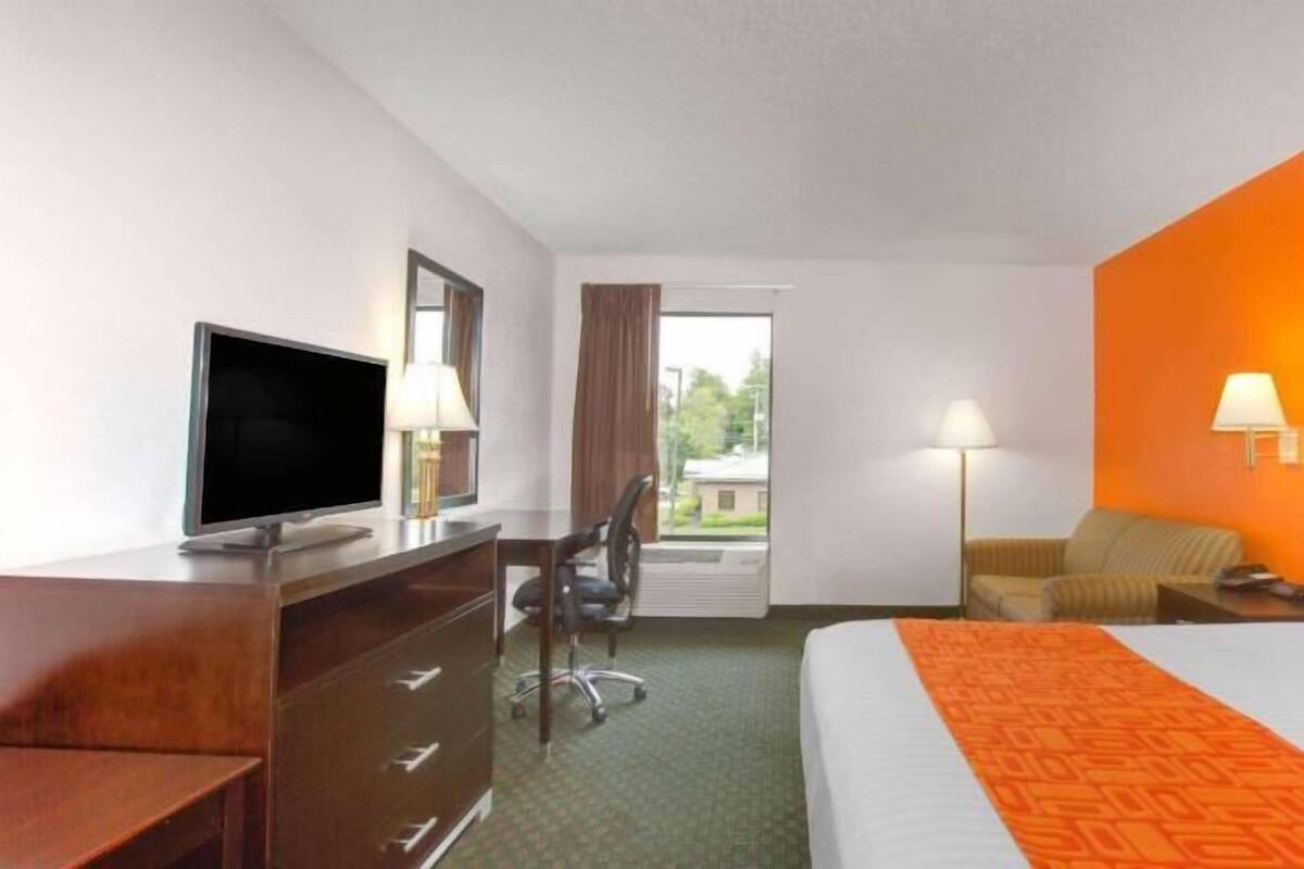 Une chambre d’hôtel équipée d’un lit, d’un bureau, d’une chaise, d’une télévision et offrant une vue sur l’extérieur.