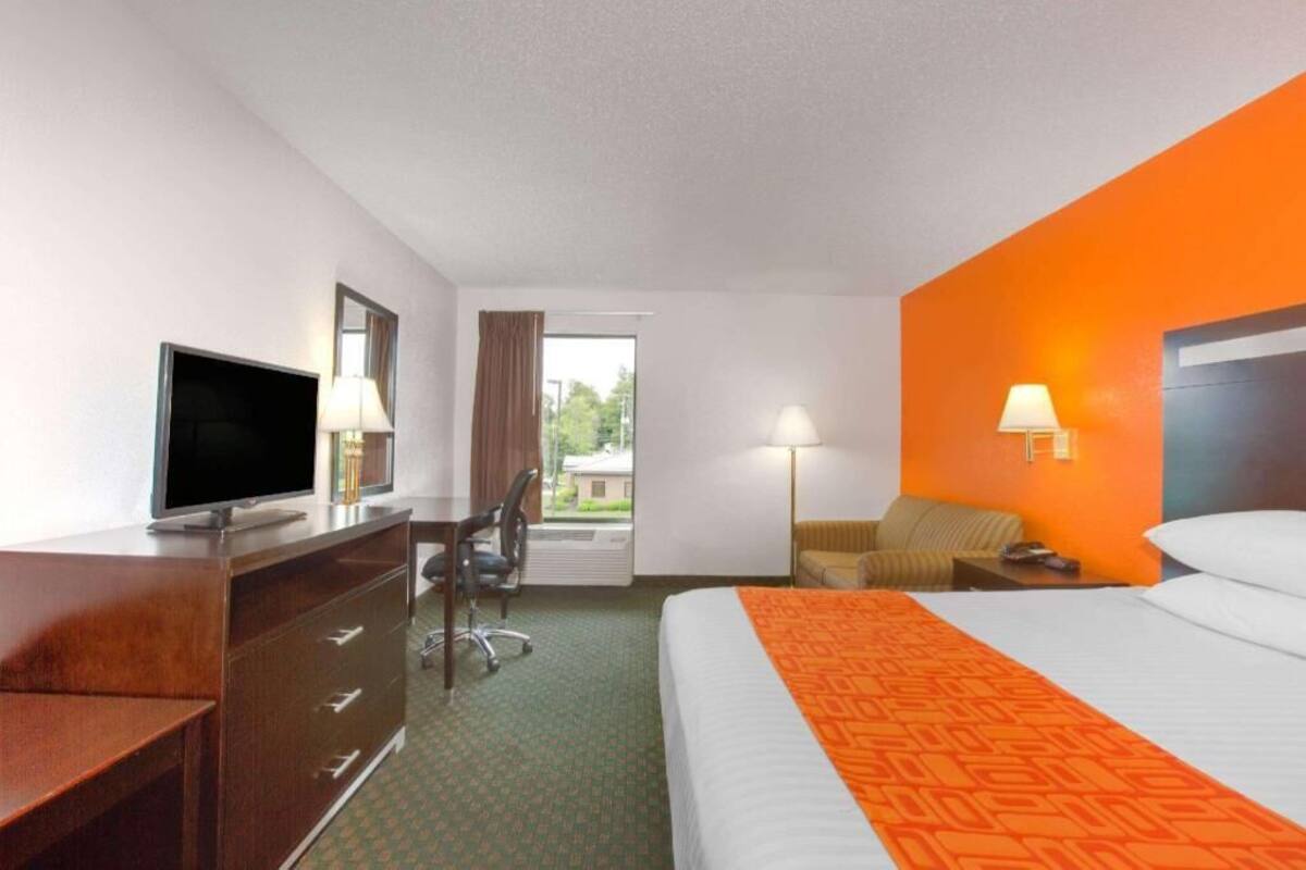 Une chambre d’hôtel avec un lit, un bureau avec une télévision, une chaise, une lampe et une vue sur l’extérieur.