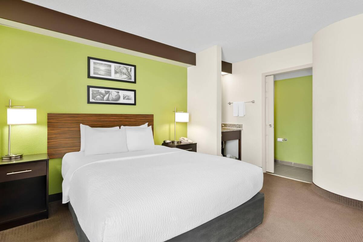 A hotel room with a large bed, two bedside lamps, a wooden headboard, and two framed pictures on the wall.