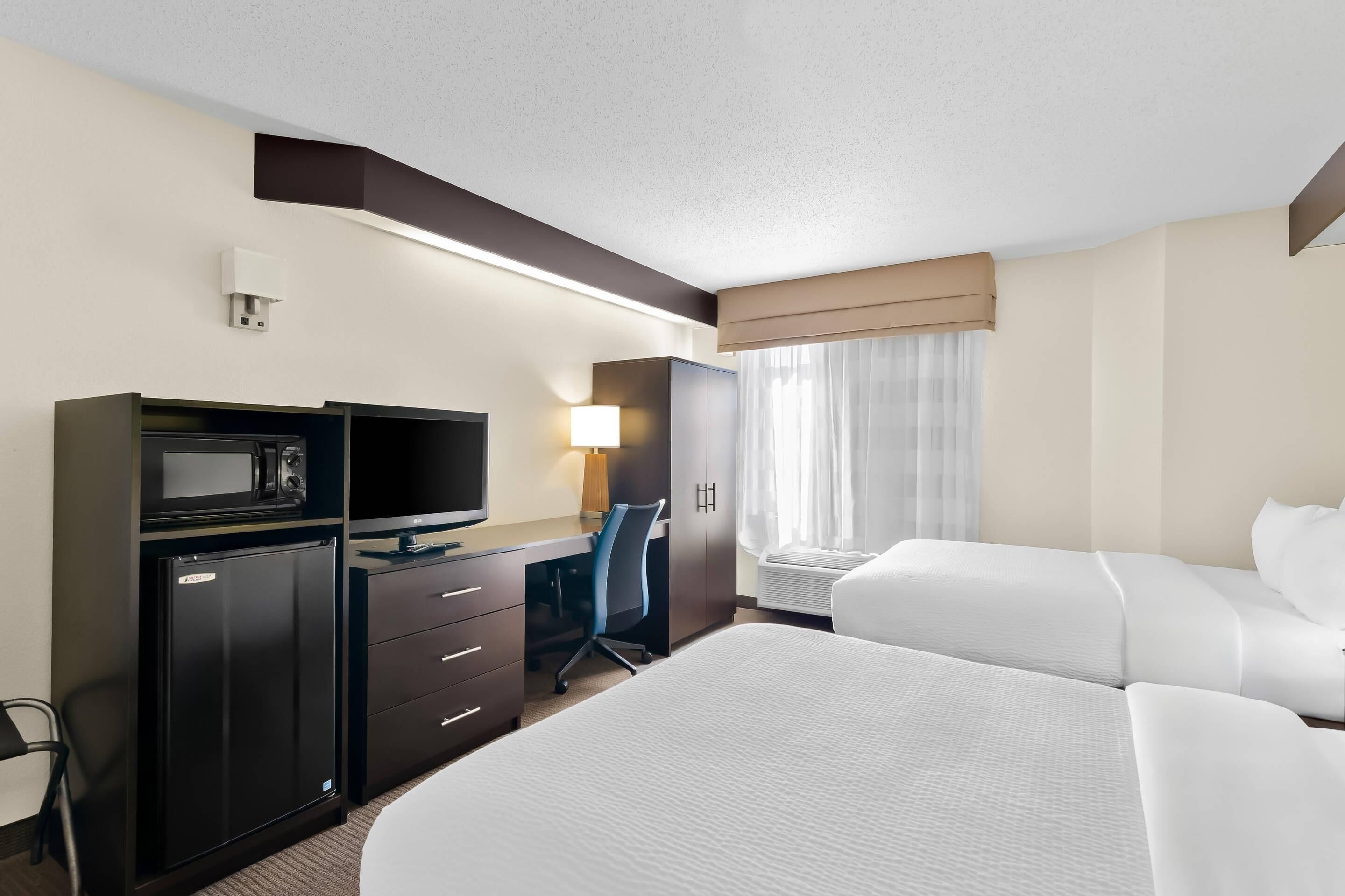 Habitación de hotel con cama, escritorio con computadora, televisor, minibar y ventana con cortinas.