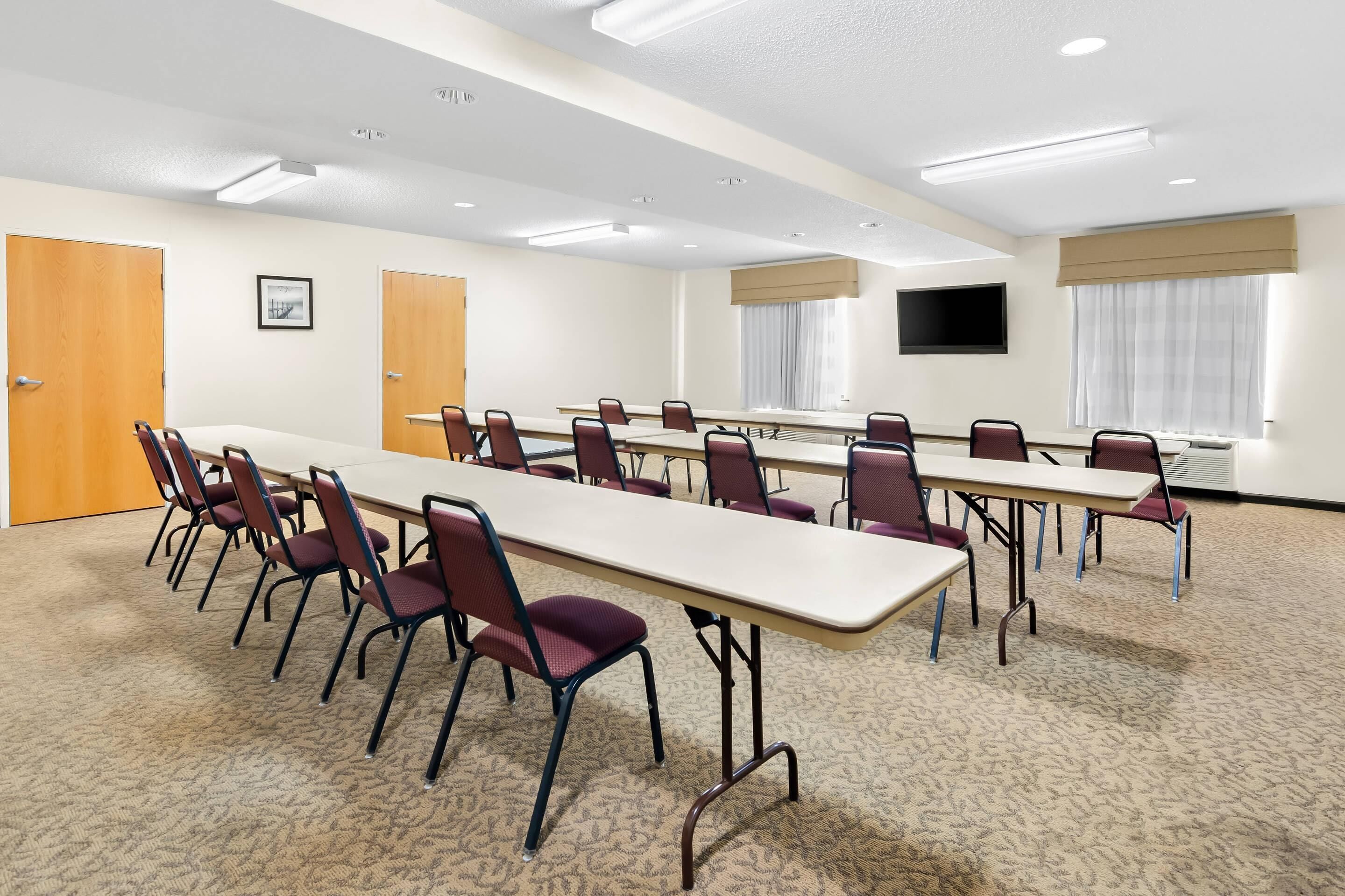 A conference room with long tables and chairs, a flat-screen TV, and a carpeted floor.