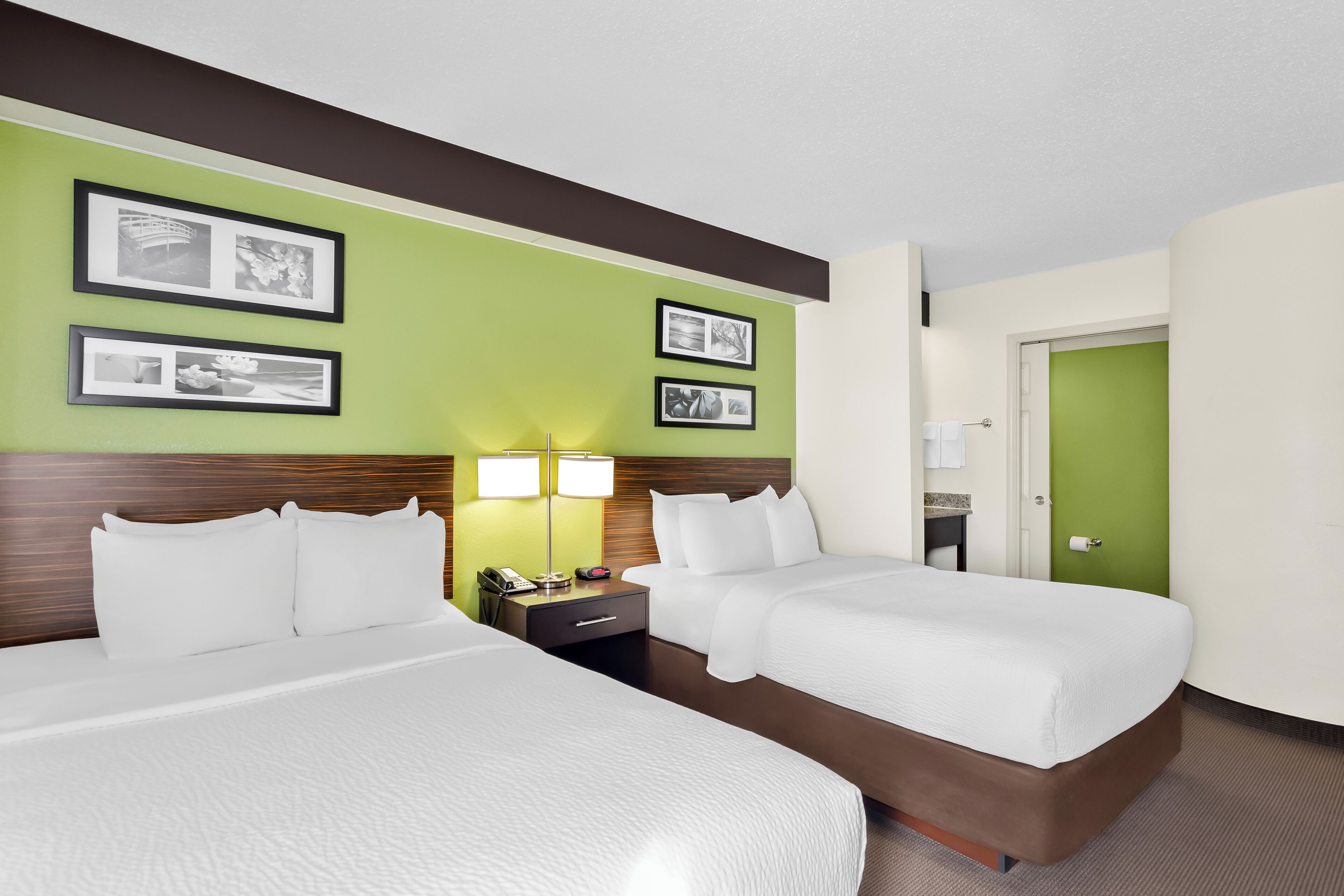 A hotel room with two beds, a nightstand with a lamp, and framed pictures on the wall.