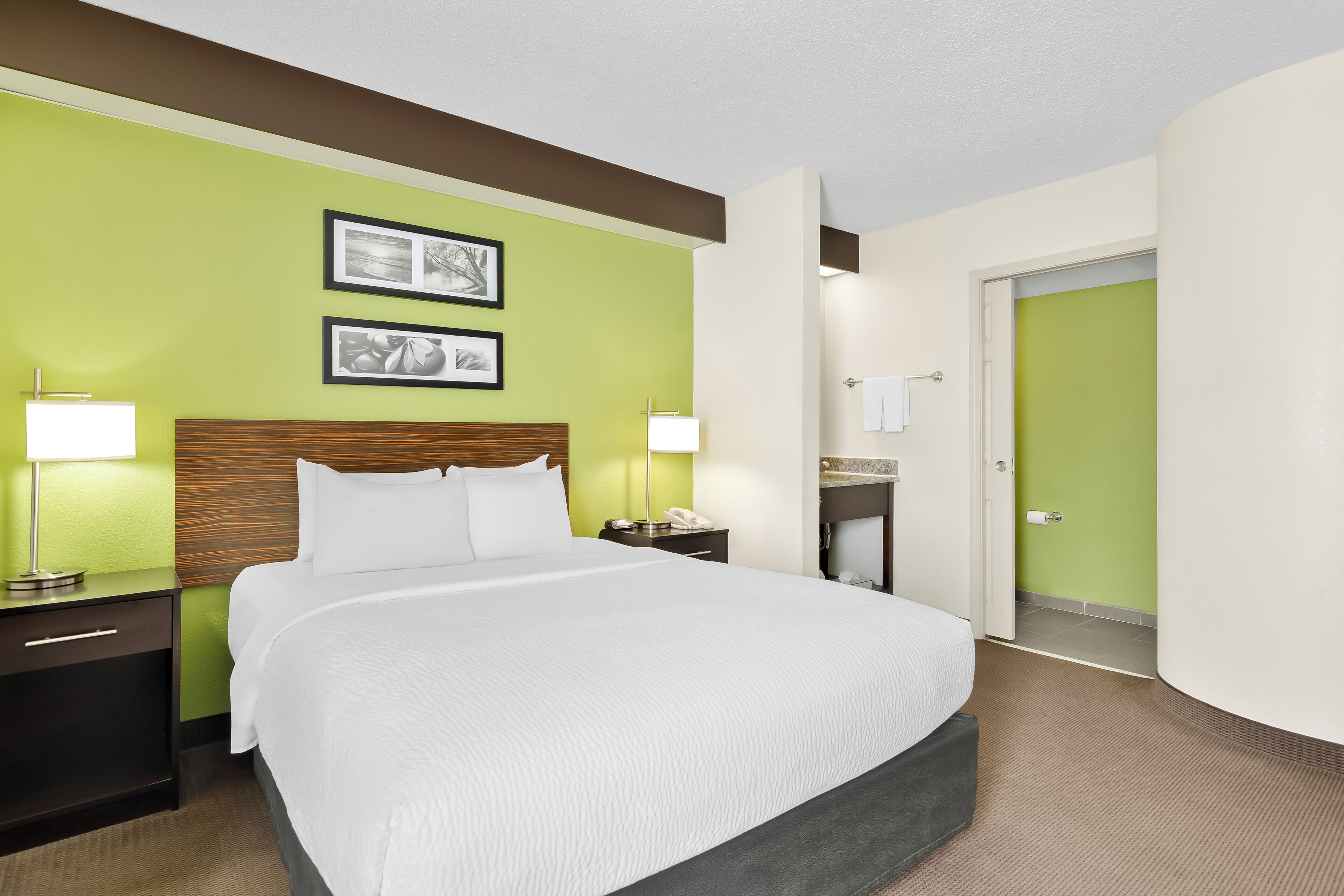Une chambre d’hôtel avec un grand lit, des tables de chevet, une petite table, une lampe et un tableau encadré au mur.